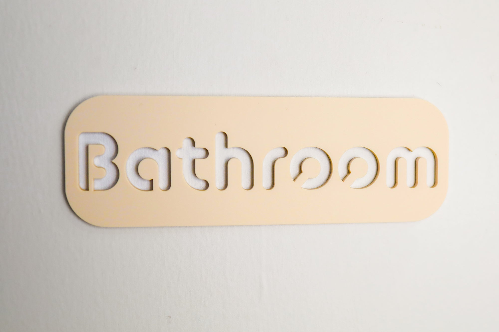 Contemporary beige bathroom door sign with cut-out text and self-adhesive backing for effortless placement